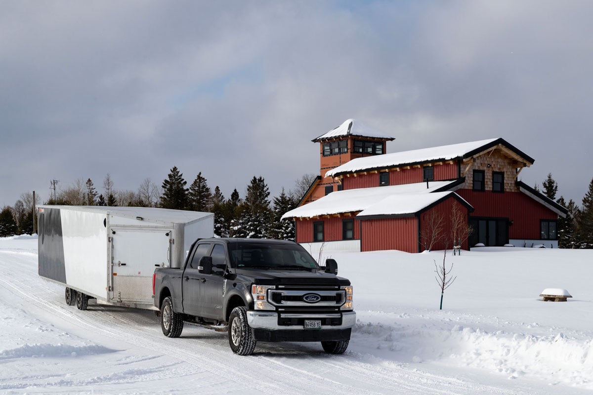 SnoPro Enclosed Deckover 6.5-Height Snow Trailers Attached To Truck With Cabins In Background SnoPro Enclosed Deckover 6.5-Height Snow Trailers Attached To Truck With Cabins In Background